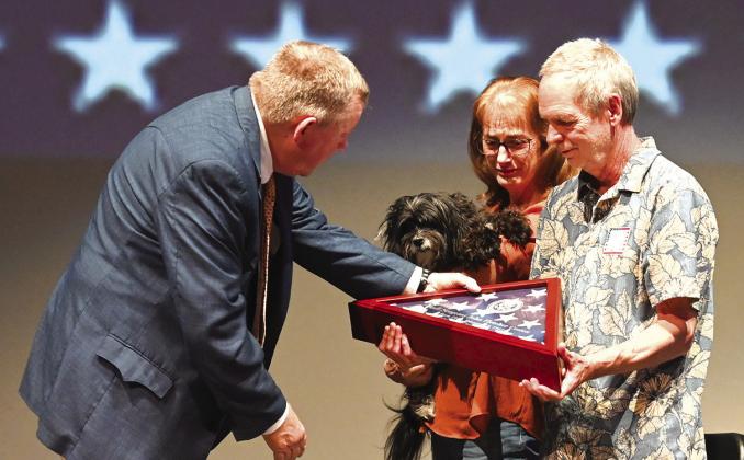 Photo Courtesy of Chisholm Country magazine Field representative for U.S. Senator John Carter, Michael McCloskey presented Robin Hill and his wife Kim and their dog Sofia with a flag flown over the U.S. Capitol in honor of Sgt. John Fletcher Coston, one of three Bosque county soldiers missing in action honored at the Missing in Action Memorial/Project Recover fundraiser Sunday, May 5, at the Clifton ISD Performance Arts Center.