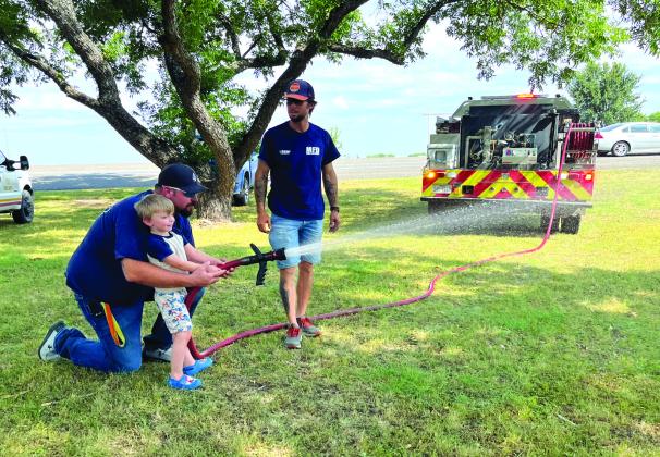 Matt Dickinson (from left) shows Lucas Dickinson how it’s done with the fire hose as Jackie Carter assists during the Meridian Volunteer Fire Department’s fundraiser at Meridian Park on Saturday, July 15. Nathan Diebenow | Meridian Tribune