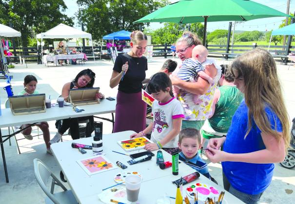 Artist Kourtney Amundson (center) taught a painting workshop during the Bosque Market for Farmers &amp; Artisans on Saturday, July 8, at Chisholm Trail Plaza in Meridian. Families from around Meridian took the opportunity to flex their creative muscles by painting a picture of flowers. Nathan Diebenow | Meridian Tribune